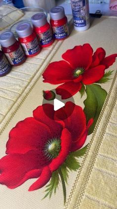 some red flowers are sitting on a table with paint bottles and thread spools