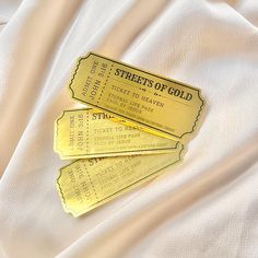 three gold tickets sitting on top of a white cloth covered in satin material with the words streets of gold written across them