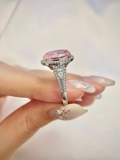 a woman's hand holding an engagement ring with a pink diamond in the center