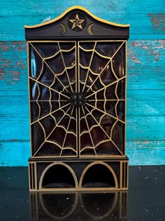 a black and gold cabinet with a spider web on it's front, against a blue wooden background