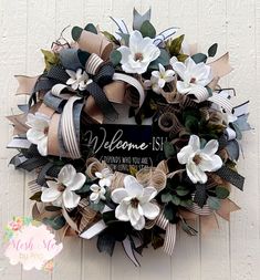 a welcome sign is attached to a wreath with white flowers and ribbons on it's front door