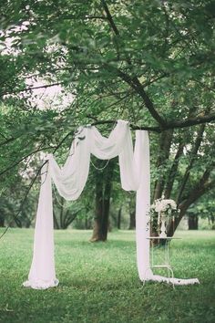 an outdoor wedding ceremony setup with white drapes and flowers on the grass under a tree