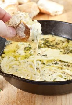 a person is dipping some food into a skillet with cheese and spinach on it