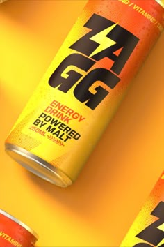 two cans of energy drink sitting next to each other on a yellow surface with orange and red colors