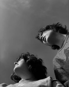 two women standing next to each other in front of a cloudy sky with one holding her head up