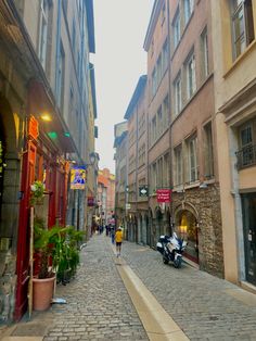 a narrow city street lined with buildings and people walking down one side, on the other