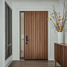 a wooden door in a white room next to a vase with orange flowers on it