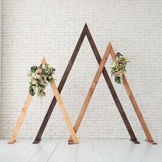 three wooden wedding archs with flowers and greenery on them in front of a white brick wall