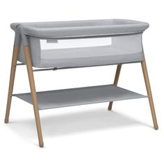 a grey baby crib with wooden legs and a shelf for changing clothes in front of it