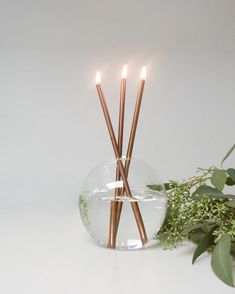 three candles are lit in a glass bowl with greenery on the table next to it