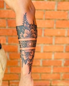 a man with a tattoo on his arm and leg is standing in front of a brick wall