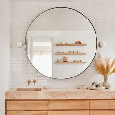 a bathroom with a large round mirror on the wall and wooden cabinets in front of it