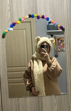 a person taking a selfie in front of a mirror wearing a bear hat and scarf