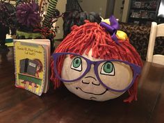 a large pumpkin with red hair and glasses sitting on a table next to a book