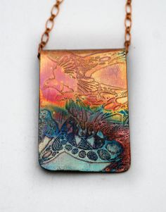 a necklace with a painting on it sitting on a white table next to a chain