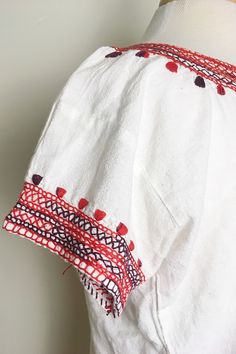 "LOVELY EMBROIDERY * short sleeves * hand embroidered * lightweight fabric * sleeve embroidery detail * red and burgundy embroidery ERA: 1970s LABEL: None SIZE: Medium bust: 42\" waist: 42\" sleeve length: 4 1/2\" length: 22\" FABRIC: feels like cotton COLOR: white, multi red color CONDITION: great, has some markings but does not affect wear" Bohemian Red Tops With Embroidered Hem, Bohemian Red Top With Embroidered Hem, Red Bohemian Top With Embroidered Hem, Bohemian Cotton Peasant Top With Tassels, Folk Style Short Sleeve Tops With Woven Motifs, Folk Style Embroidered Peasant Top For Vacation, Summer Cotton Peasant Top With Intricate Embroidery, Folk Style Top With Woven Motifs And Short Sleeves, Traditional Embroidered Peasant Top For Beach