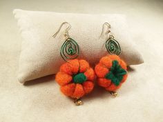 two orange and green pom - poms are sitting on a white pillow next to a pair of earrings