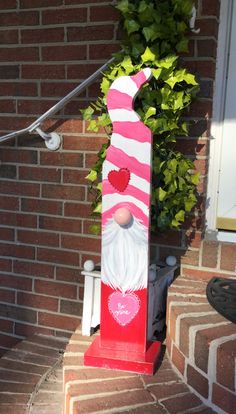 a red and white statue with a pink heart on it's face sitting in front of a brick building