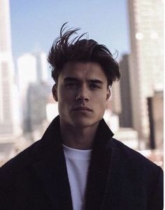 a young man standing in front of a cityscape with tall buildings behind him