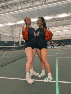 two young women standing on a tennis court giving the peace sign with their hands in front of them