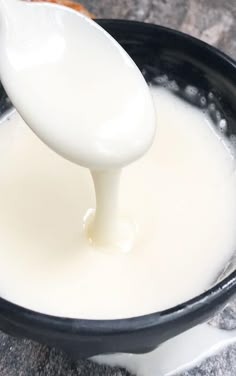 a spoon full of milk being poured into a black bowl on top of a counter