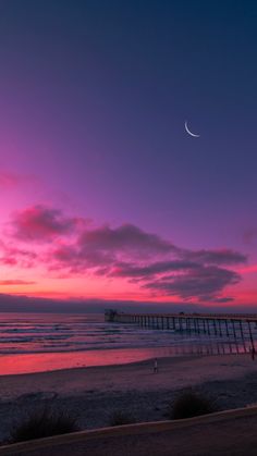 the sun is setting at the beach with a pier in the background