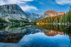 the mountains are reflected in the still water on the lake's surface, with pine trees lining the shore