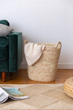 a green couch sitting next to a basket on top of a wooden floor in front of a white wall