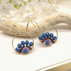 a pair of earrings with blue beads and gold hoops sitting on a white surface