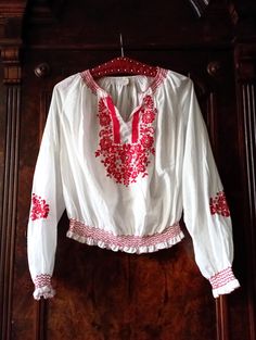 Beautiful 1980s Vintage Hungarian embroidered blouse. White airy fabric with embroidered flowers and vines in a vibrant shade of red on the front and the sleeves. Red zic-zac stitching around the neckline and cuffs. Split neckline. Wide raglan sleeves. Smocked elasticated waist with red zic-zac stitching. Press button closure on the waist. Traditional Hungarian blouses will always be a staple for Bohemians. Looks great with a a pair of highwaist flared jeans and brown clogs! BRAND: No brand labe Spring Folk Embroidered Peasant Top, Summer Folk Peasant Top With Embroidered Sleeves, Folk Style Long Sleeve Embroidered Top For Summer, Folk Style Embroidered Long Sleeve Top For Summer, Spring Folk Style Peasant Tunic Top, Spring Folk Peasant Tunic Top, Long Sleeve Embroidered Top For Spring Festival, Spring Folk Tunic Peasant Top, Long Sleeve Peasant Top For Festivals