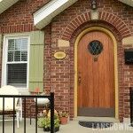 a brick house with green shutters and a wooden door on the front porch, surrounded by white lawn chairs