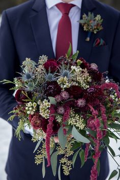 a man in a suit holding a bouquet of flowers and greenery on his lapel