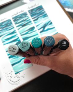 a person holding five different colored markers in their hand, with the numbers on them