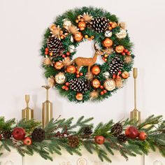 a christmas wreath on top of a mantle with pine cones and ornaments hanging from it