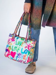 a woman carrying a colorful handbag with the words love on it and hearts all over it