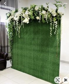 a green backdrop with white flowers and greenery on it in the middle of a room