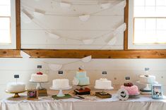 a table topped with lots of cakes and desserts next to a wall hanging from the ceiling