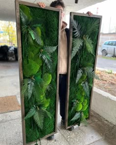 a man is holding up two large green panels with plants on them in front of him