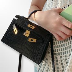 Color: Black.
 	Matte Alligator Pattern Leather.
 	Chévre Goatskin leather lining.
 	Gold finished hardware.
 	Turn over flap lock.
 	Single rolled top handle.
 	Removable leather strap.
 	Hand, Shoulder and Crossbody Carry.
 	Inside flat pocket.
 	Size: 19 cm.
 	Made in France.
 	Hermes Box, dust bag and documents included. Alligator Pattern, Mini Kelly, Kelly Sellier, Hermes Box, Black Matte, Pocket Size, Gold Finish, Alligator, Top Handle