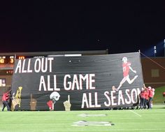 an all out game banner on the sidelines at a football game with players in red and black uniforms