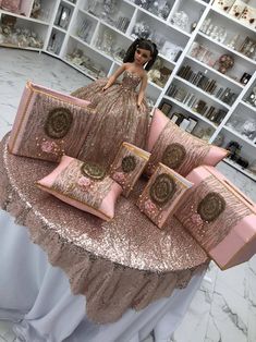 a barbie doll sitting on top of a table with pink pillows and decorative pillow cases