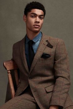 a young man in a suit sitting on a chair with his hands in his pockets