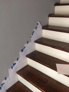 some white and blue tape is on the stair treads that are painted with dark wood