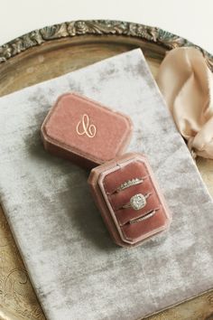 two pink velvet jewelry boxes sitting on top of a silver tray next to a white napkin