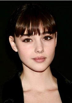 a close up of a person wearing a black jacket and brown hair with bangs on her head