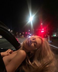 a woman sitting in the driver's seat of a car on a street at night