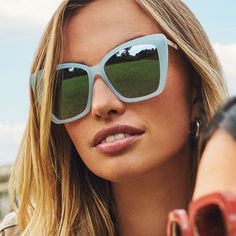 a woman wearing sunglasses with trees reflected in the lenses on her face and looking off to the side