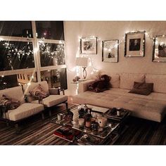 a living room filled with furniture next to a window covered in lights and framed pictures