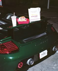 the back end of a green sports car with food and drinks on it's trunk