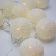 some white balls are sitting next to each other on a table with string lights around them